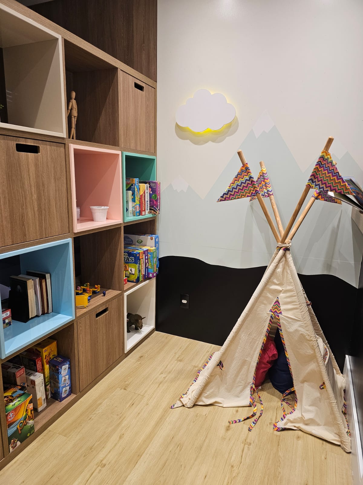 Espaço infantil do consultório com cabana, luminária em formato de nuvem e estante colorida