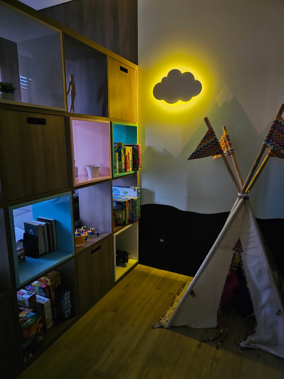 Espaço infantil com iluminação suave, cabana e parede decorada com montanhas