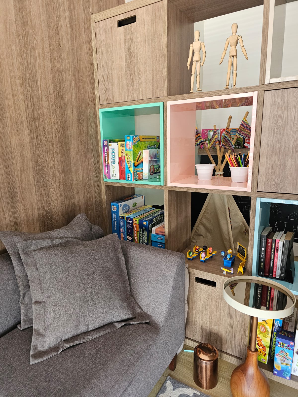 Detalhe da poltrona cinza ao lado de estante com livros, jogos e materiais terapêuticos